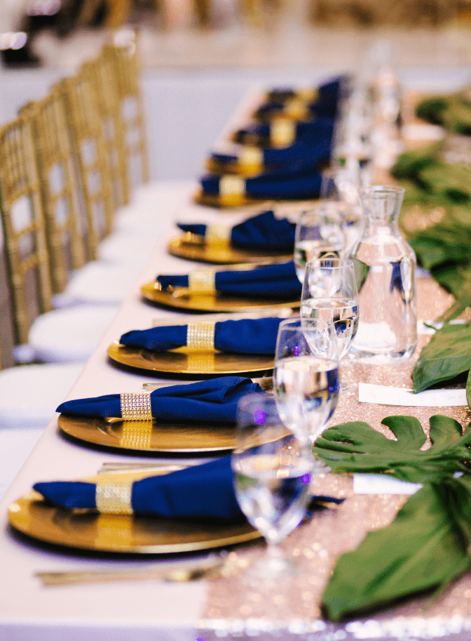 Reception table set with gold chargers, navy napkins and greenery
