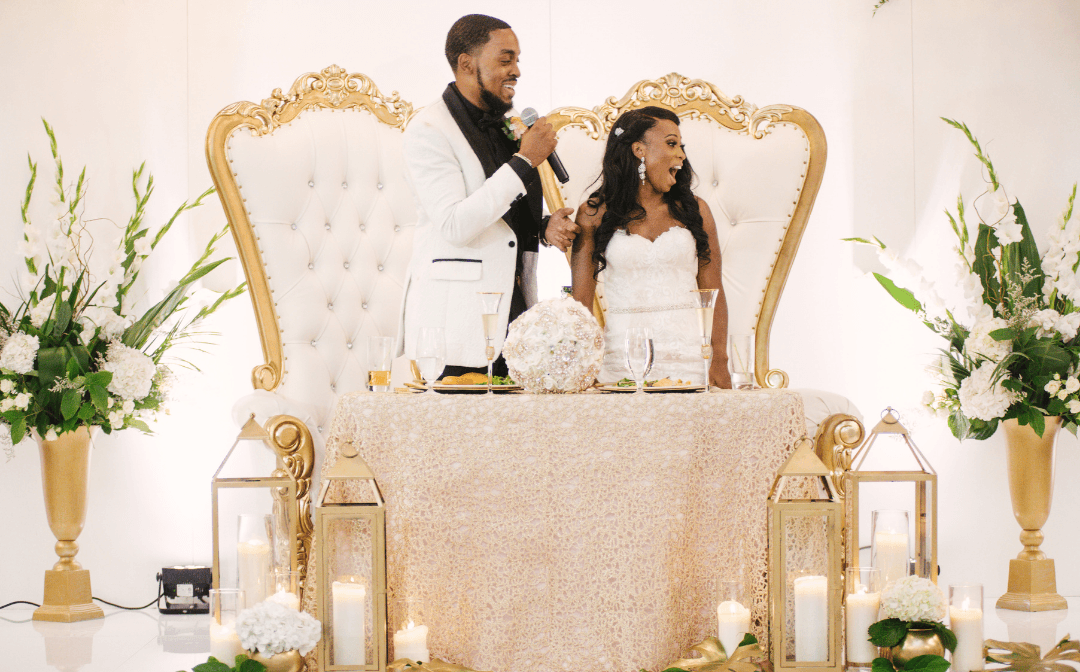 Bride and groom seated on gold thrones at their sweetheart table