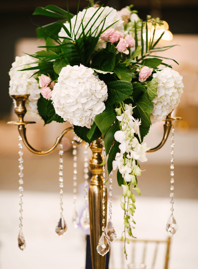 Tall centerpiece of white hydrangeas and greenery on a gold candelabra