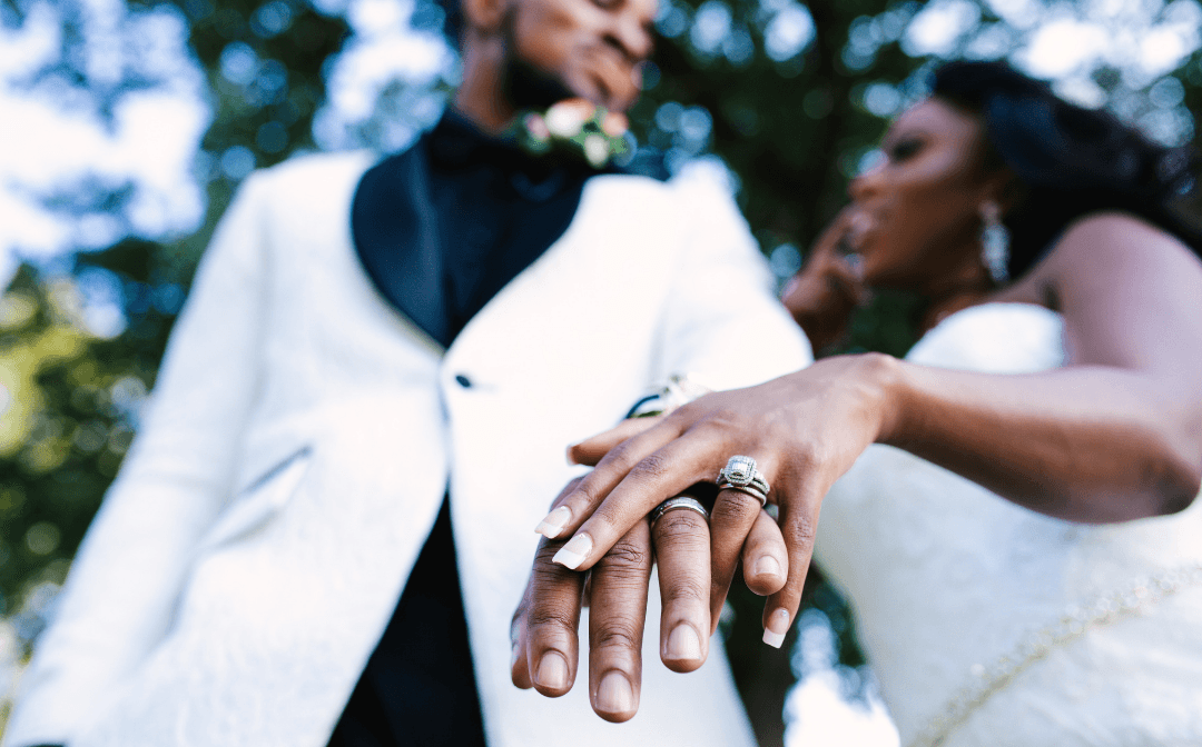 Groom in a white jacket holding his bride's hand, showing her ring