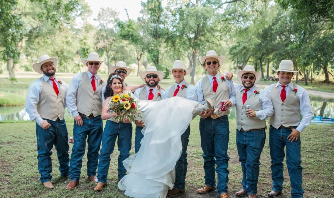 Bride with groomsmen in cowboy hats, jeans and red ties on a lawn