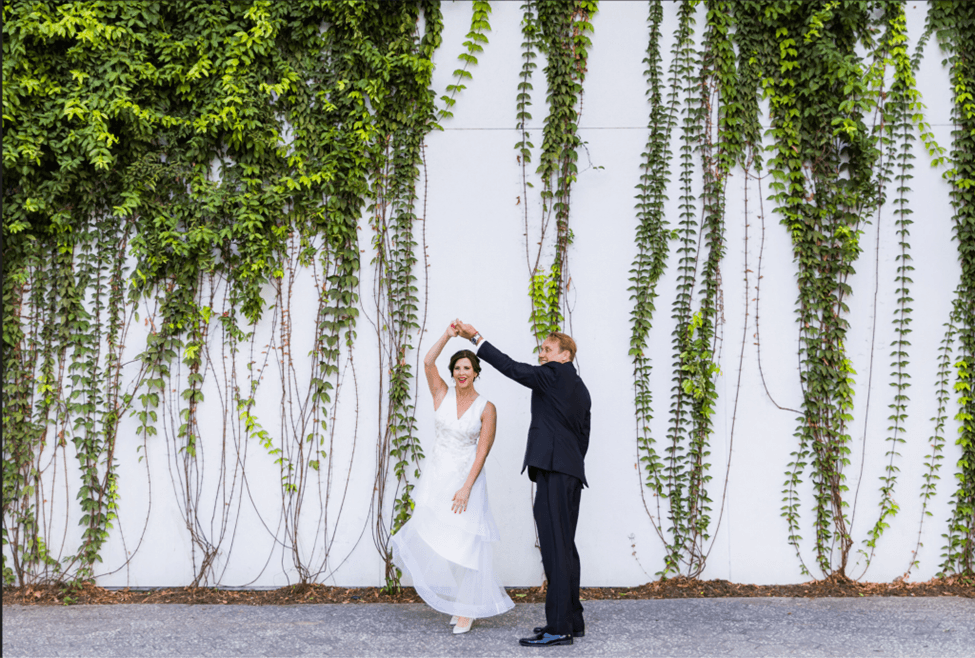 Bride and groom dancing in front of a white wall draped with greenery