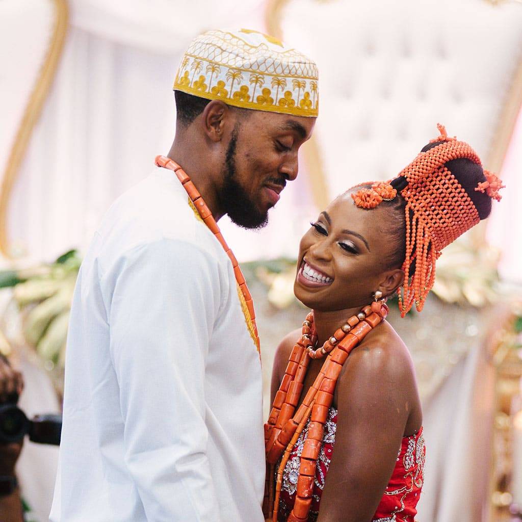 Bride and groom in coral beads and traditional wedding attire, smiling at each other