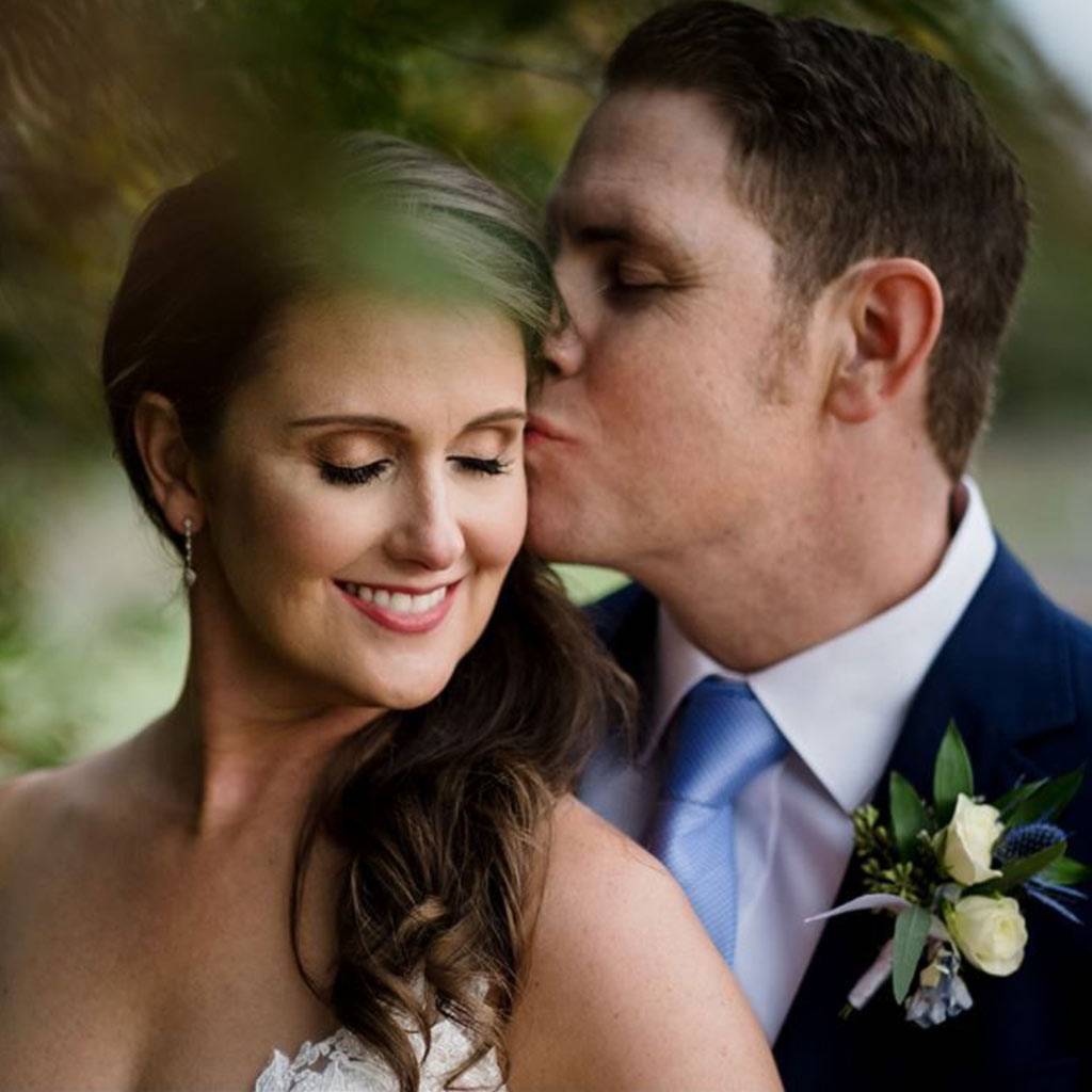 Groom kissing his smiling bride on the temple