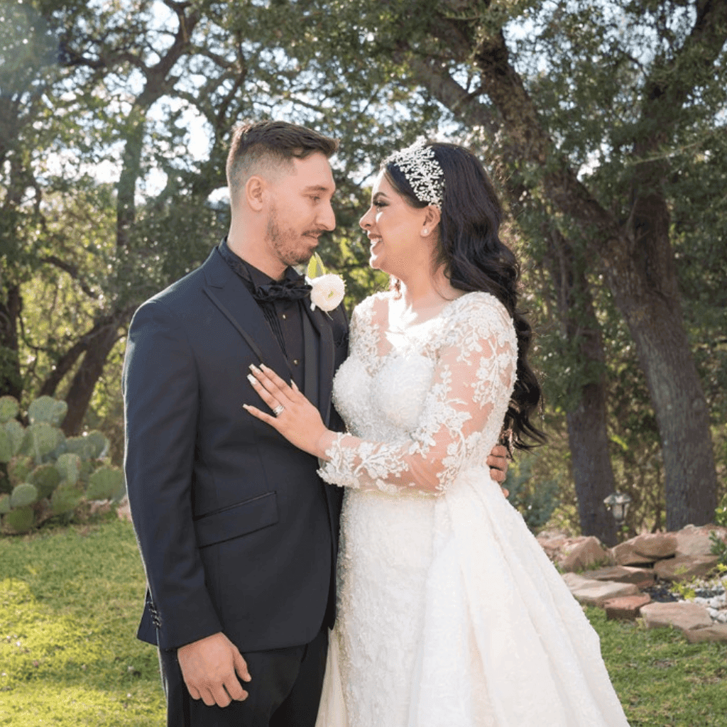 Bride in a lace gown and tiara with her hand on her groom's chest, under oak trees