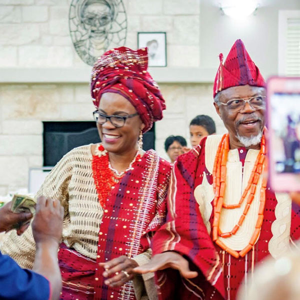 Couple in matching red and gold traditional attire smiling at a celebration