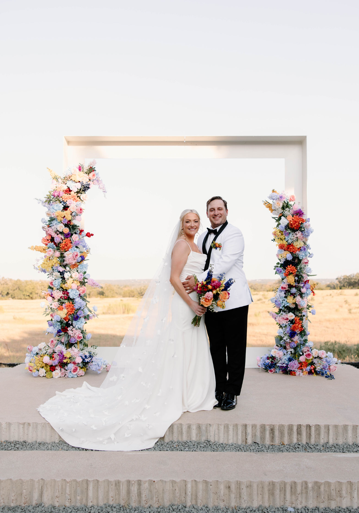 Bride and groom standing between two tall floral columns at an outdoor ceremony site