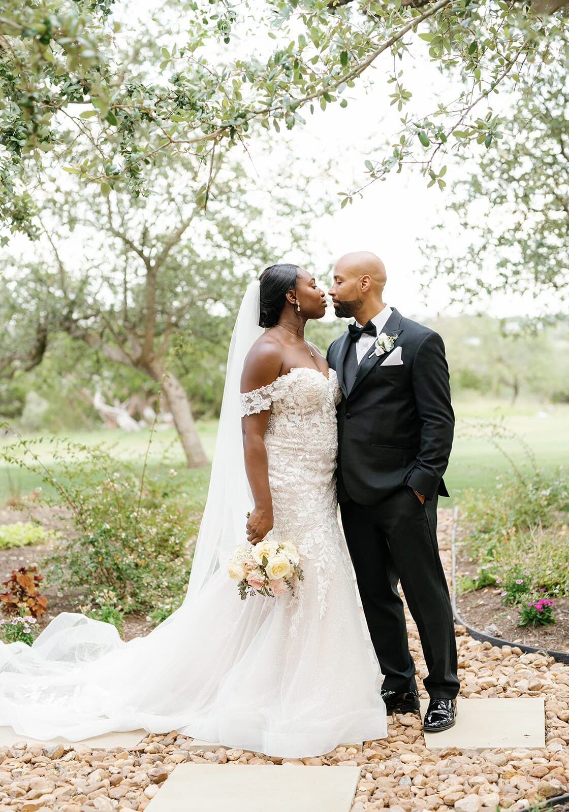 Alfredo + Motola | Canyonwood Ridge Bride and groom kissing on a garden path under oak trees