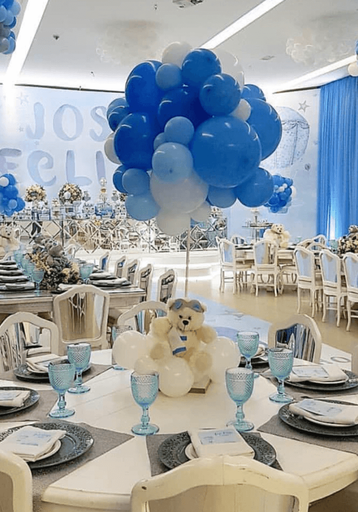 Banquet room set for a baby shower with blue balloon clusters and a teddy bear centerpiece