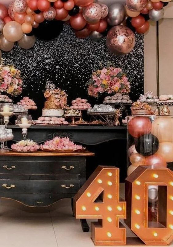 Birthday dessert table with a balloon arch and a lighted number 40